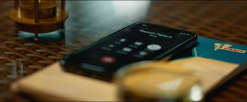 Movie still from “Home” (2021), directed by Saalih Chaudhry – A phone sitting on top of a wooden table next to a cup; Extreme Close Up shot, High angle