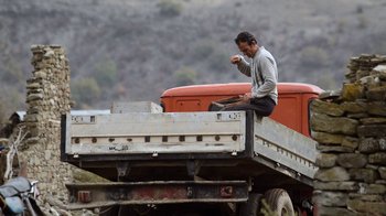 Movie still from “Honeyland” (2019), directed by Tamara Kotevska – A man sitting on the back of a red truck; Wide shot, High angle