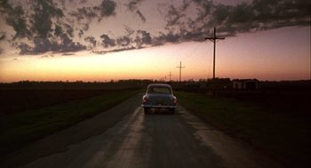 Movie still from “Hoosiers” (1986), directed by David Anspaugh – A car driving down a road at sunset; Extreme Wide shot, Low angle