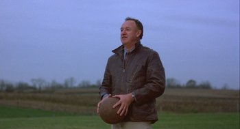 Movie still from “Hoosiers” (1986), directed by David Anspaugh – A man in a brown jacket holding a brown ball; Medium shot, Low angle