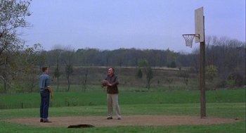 Movie still from “Hoosiers” (1986), directed by David Anspaugh – A man standing on a baseball field holding a ball; Extreme Wide shot, Over the shoulder angle