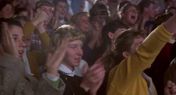 Movie still from “Hoosiers” (1986), directed by David Anspaugh – A group of people sitting in a room clapping; Medium shot, High angle