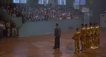 Movie still from “Hoosiers” (1986), directed by David Anspaugh – A group of people standing on a basketball court in front of an audience; Extreme Wide shot, High angle
