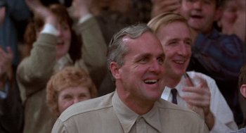 Movie still from “Hoosiers” (1986), directed by David Anspaugh – A group of people sitting in a crowd and smiling; Close Up shot, Over the shoulder angle