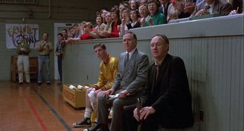 Movie still from “Hoosiers” (1986), directed by David Anspaugh – A group of men sitting in front of an audience; Wide shot, Over the shoulder angle