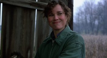 Movie still from “Hoosiers” (1986), directed by David Anspaugh – A woman in a green jacket smiling for the camera; Close Up shot, Low angle