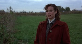 Movie still from “Hoosiers” (1986), directed by David Anspaugh – A woman standing in a grassy field wearing a red coat; Close Up shot, Over the shoulder angle