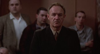 Movie still from “Hoosiers” (1986), directed by David Anspaugh – A man in a suit and tie standing in front of other men; Close Up shot, Low angle