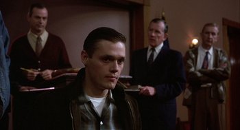 Movie still from “Hoosiers” (1986), directed by David Anspaugh – A man standing next to another man in a suit; Medium shot, Over the shoulder angle
