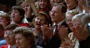 Movie still from “Hoosiers” (1986), directed by David Anspaugh – An older man and woman are clapping in a crowd; Close Up shot, High angle