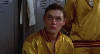 Movie still from “Hoosiers” (1986), directed by David Anspaugh – A man in a yellow jacket sitting in a locker room; Close Up shot, Low angle