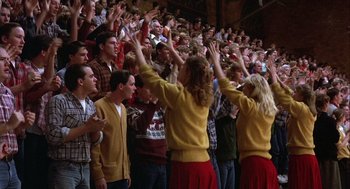 Movie still from “Hoosiers” (1986), directed by David Anspaugh – A group of people standing in front of an audience raising their hands; Wide shot, High angle