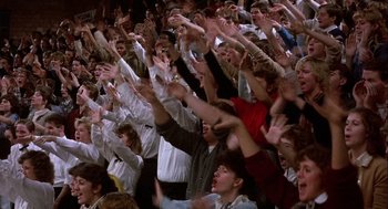 Movie still from “Hoosiers” (1986), directed by David Anspaugh – A group of people standing in a stadium with their hands up; Extreme Wide shot, High angle