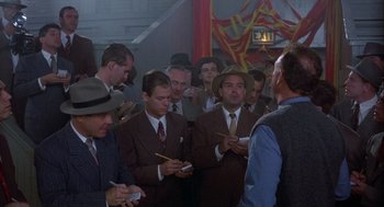 Movie still from “Hoosiers” (1986), directed by David Anspaugh – A group of men standing around each other in a room; Wide shot, High angle