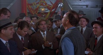 Movie still from “Hoosiers” (1986), directed by David Anspaugh – A group of men standing in a room; Medium shot, Over the shoulder angle