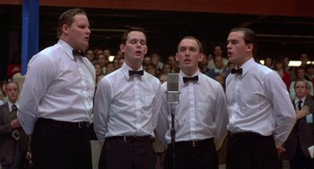 Movie still from “Hoosiers” (1986), directed by David Anspaugh – A group of young men singing in front of an audience; Medium shot, Low angle