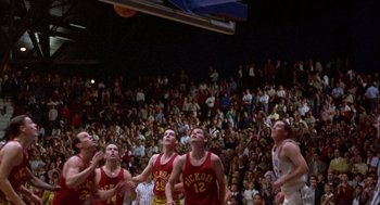 Movie still from “Hoosiers” (1986), directed by David Anspaugh – A group of young men playing a game of basketball in front of an audience; Wide shot, Overhead angle
