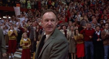 Movie still from “Hoosiers” (1986), directed by David Anspaugh – A man standing in front of a crowd of onlookers; Medium shot, Over the shoulder angle