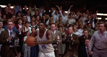 Movie still from “Hoosiers” (1986), directed by David Anspaugh – A group of people watching a basketball game in front of an audience; Medium shot, High angle