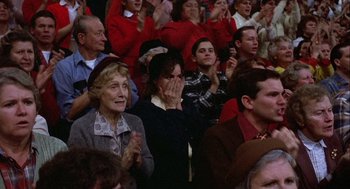 Movie still from “Hoosiers” (1986), directed by David Anspaugh – A group of people sitting in a crowd clapping; Medium shot, Over the shoulder angle