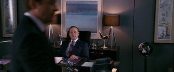 Movie still from “Horrible Bosses” (2011), directed by Seth Gordon – A man sitting at a desk in front of a lamp; Medium shot, Over the shoulder angle