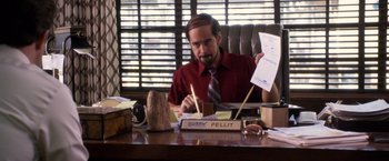 Movie still from “Horrible Bosses” (2011), directed by Seth Gordon – A man sitting at a desk with papers on a table; Medium shot, Over the shoulder angle