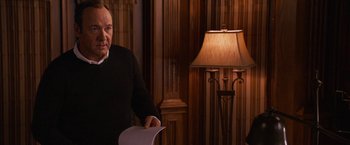 Movie still from “Horrible Bosses” (2011), directed by Seth Gordon – An older man holding papers in front of a lamp in a living room; Medium shot, Over the shoulder angle