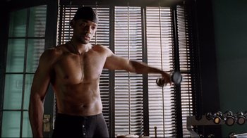 Movie still from “I, Robot” (2004), directed by Alex Proyas – A shirtless man holding a pair of shoes in a room; Medium shot, Over the shoulder angle