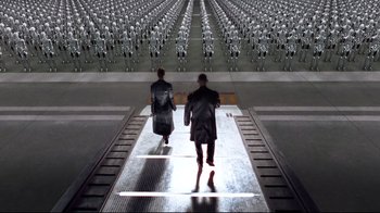 Movie still from “I, Robot” (2004), directed by Alex Proyas – Two people are walking down a ramp in front of a lot of robots; Extreme Wide shot, High angle