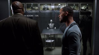 Movie still from “I, Robot” (2004), directed by Alex Proyas – Two men are standing in front of a table; Medium shot, Over the shoulder angle
