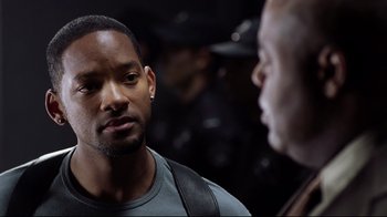Movie still from “I, Robot” (2004), directed by Alex Proyas – A man in a gray t - shirt is talking to another man in a black shirt; Close Up shot, Over the shoulder angle