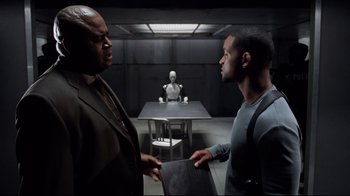 Movie still from “I, Robot” (2004), directed by Alex Proyas – Two men talking to each other in front of a robot; Medium shot, Over the shoulder angle