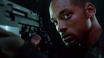 Movie still from “I, Robot” (2004), directed by Alex Proyas – A man holding a gun while wearing a black shirt; Close Up shot, Low angle