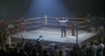 Movie still from “Hot Shots!” (1991), directed by Jim Abrahams – A man in a boxing ring with a crowd watching; Extreme Wide shot, High angle