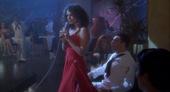 Movie still from “Hot Shots!” (1991), directed by Jim Abrahams – A woman in a long red dress holding a microphone; Wide shot, High angle