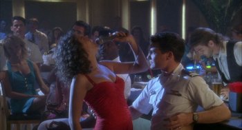 Movie still from “Hot Shots!” (1991), directed by Jim Abrahams – A woman in a red dress is drinking from a bottle; Medium shot, Over the shoulder angle