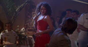 Movie still from “Hot Shots!” (1991), directed by Jim Abrahams – A woman in a red dress is holding a microphone; Medium shot, Over the shoulder angle