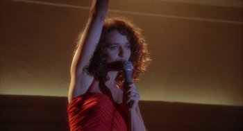 Movie still from “Hot Shots!” (1991), directed by Jim Abrahams – A woman in a red dress is holding a microphone; Medium shot, Low angle