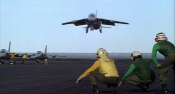 Movie still from “Hot Shots!” (1991), directed by Jim Abrahams – Two men are standing on a runway as a fighter jet flies overhead; Wide shot, Low angle