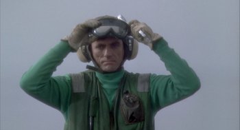 Movie still from “Hot Shots!” (1991), directed by Jim Abrahams – A man in green shirt and goggles holding his helmet; Close Up shot, Low angle