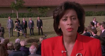 Movie still from “Hot Shots! Part Deux” (1993), directed by Jim Abrahams – A woman in a red jacket standing in front of a group of people; Close Up shot, Over the shoulder angle