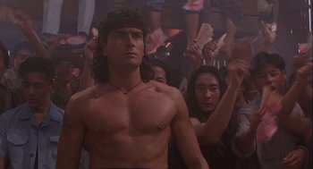 Movie still from “Hot Shots! Part Deux” (1993), directed by Jim Abrahams – A man in a crowd of people with his hands raised; Medium shot, Low angle