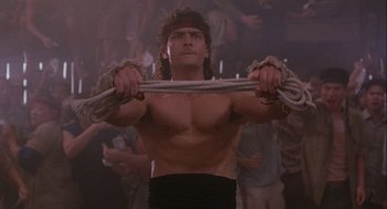 Movie still from “Hot Shots! Part Deux” (1993), directed by Jim Abrahams – A man holding a rope while standing in front of a group of people; Medium shot, Low angle