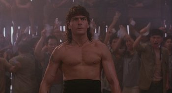 Movie still from “Hot Shots! Part Deux” (1993), directed by Jim Abrahams – A man in a black shirt is in front of a group of people; Medium shot, Low angle