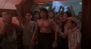 Movie still from “Hot Shots! Part Deux” (1993), directed by Jim Abrahams – A group of people standing around a man with no shirt on; Medium shot, Low angle
