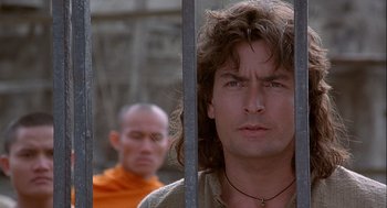 Movie still from “Hot Shots! Part Deux” (1993), directed by Jim Abrahams – A man with long curly hair is behind bars; Close Up shot, Over the shoulder angle