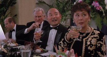 Movie still from “Hot Shots! Part Deux” (1993), directed by Jim Abrahams – A group of people sitting at a dinner table drinking wine; Medium shot, High angle
