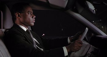 Movie still from “Hot Shots! Part Deux” (1993), directed by Jim Abrahams – A man sitting in a car holding a steering wheel; Medium shot, Low angle