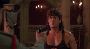 Movie still from “Hot Shots! Part Deux” (1993), directed by Jim Abrahams – A man holding a gun while wearing a tank top; Medium shot, Over the shoulder angle