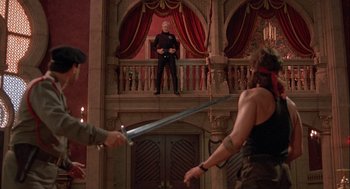 Movie still from “Hot Shots! Part Deux” (1993), directed by Jim Abrahams – A man sitting on top of a balcony holding a sword; Wide shot, Over the shoulder angle